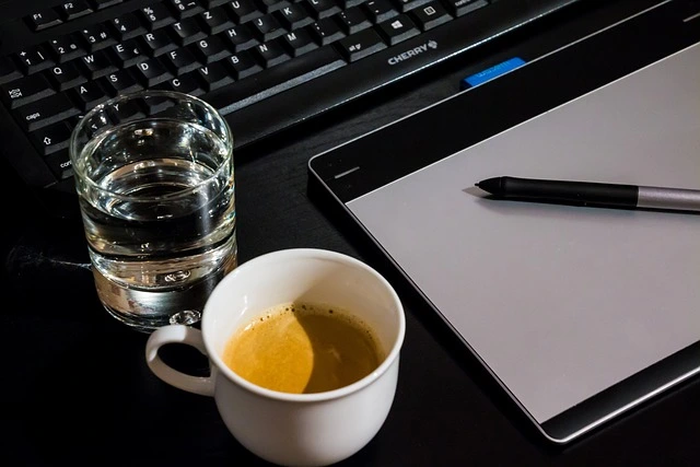 Tavoletta grafica con penna, tastiera e tazza di caffè su una scrivania nera
