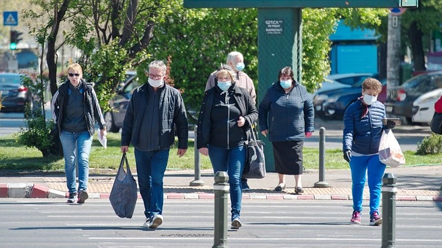 Persone con la mascherina che attraversano la strada con le borse della spesa